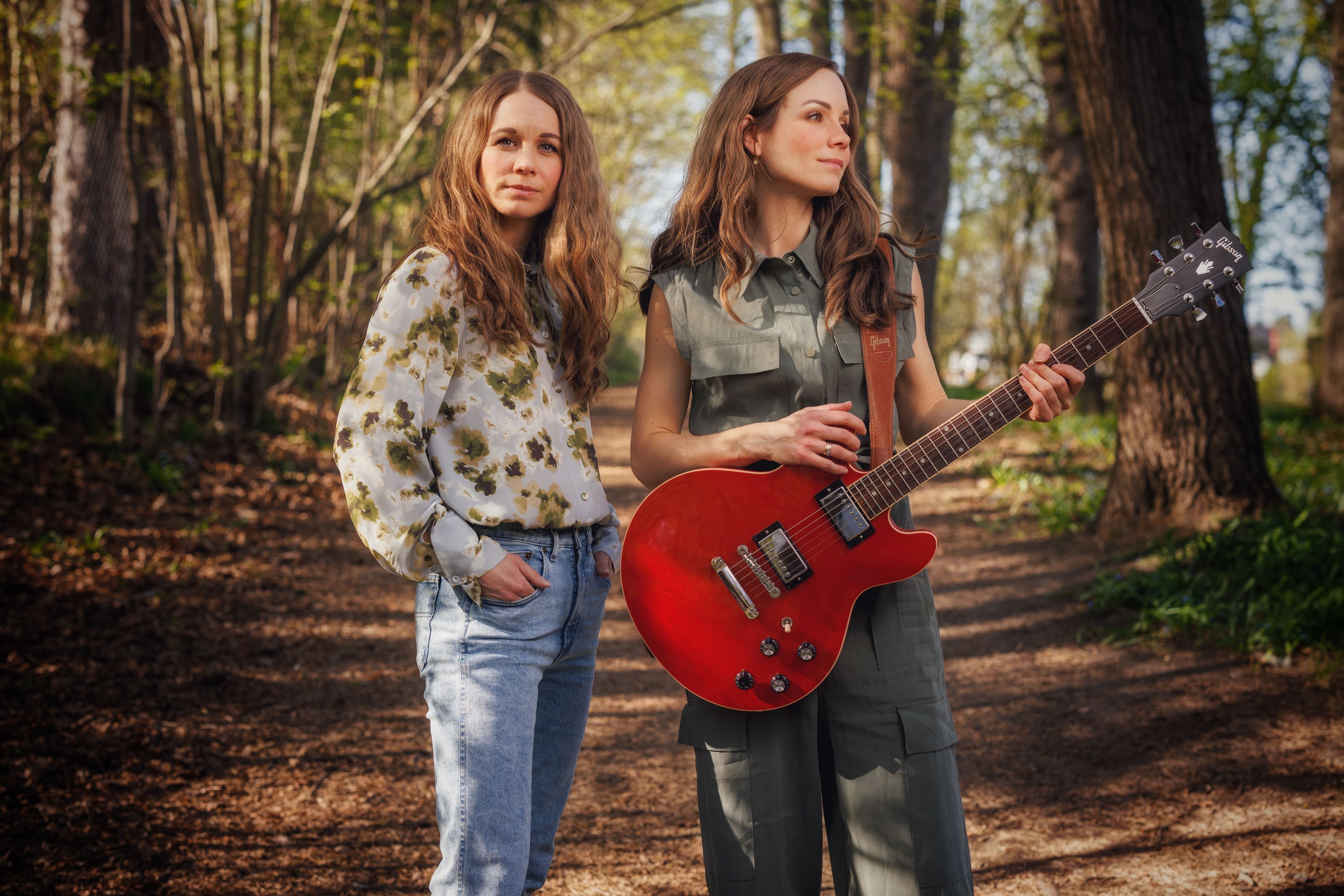 Ingelin and Hildegunn posing in the forest, Ingelin holding a red electric guitar